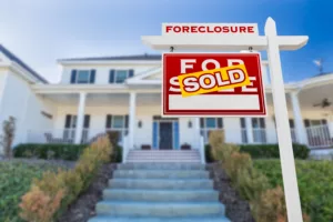 A house with a foreclosure sign with a "Sold" sticker on top- Junk-A-Haulics